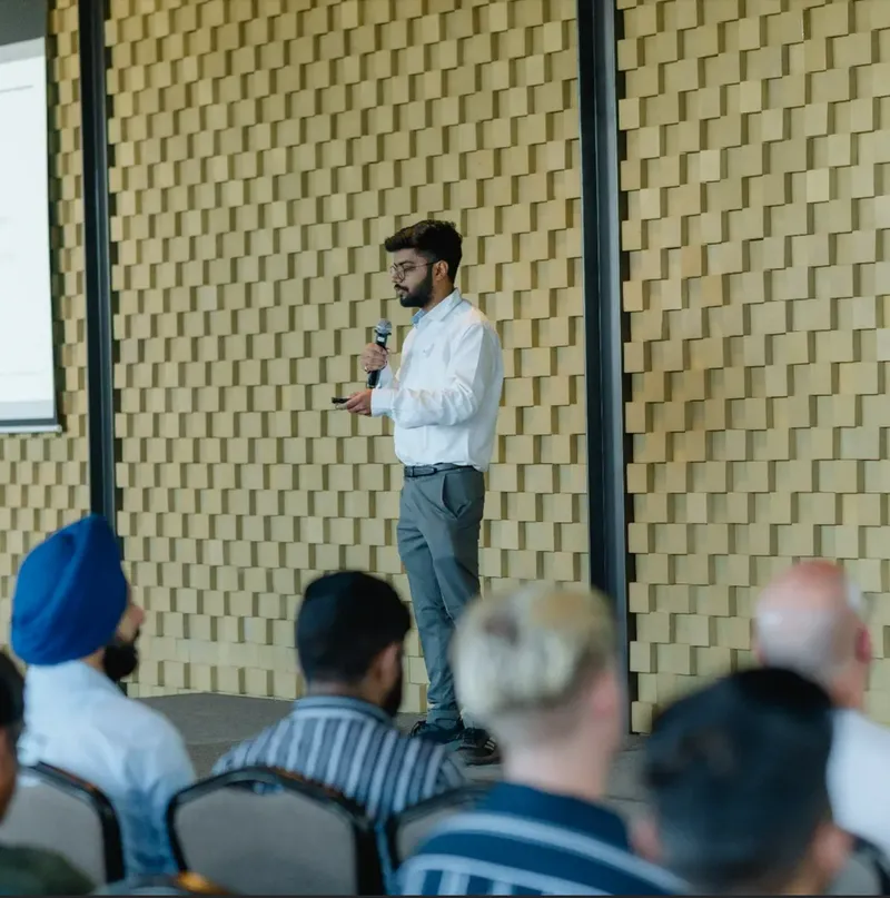 Shaurya Jain speaking at an SEO conference, standing on stage with a microphone in front of a seated audience